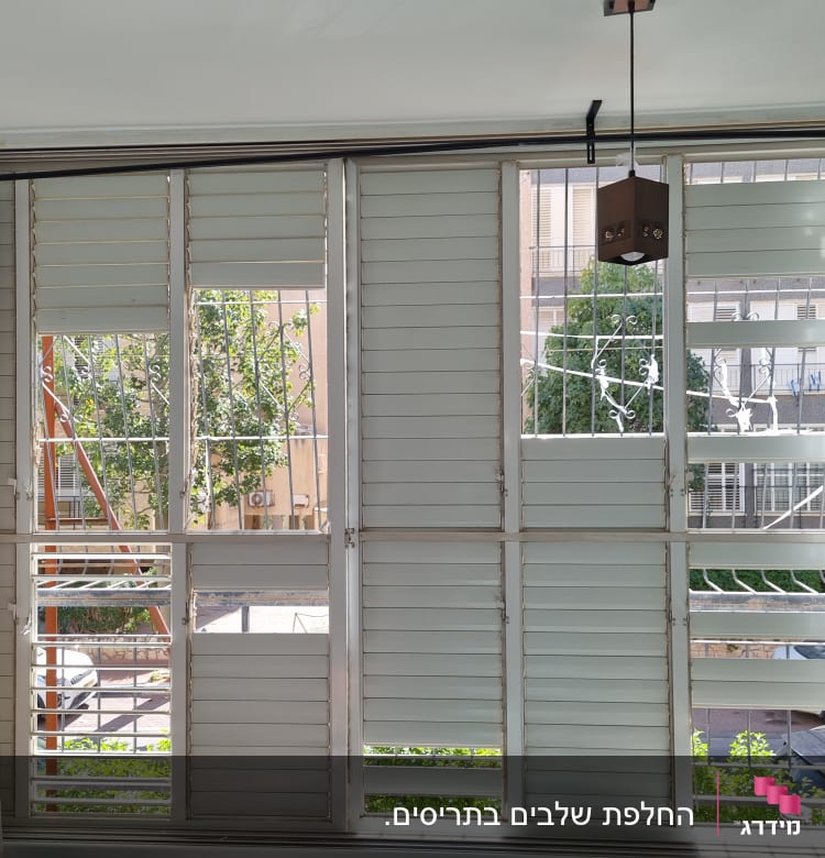 תריסים לבנים עם סורגים בחלון גדול